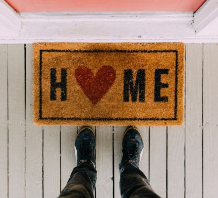 Person standing in front of a house with a door mat that says HOME